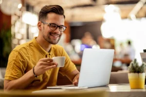 Homem tomando um café enquanto olha para seu notebook
