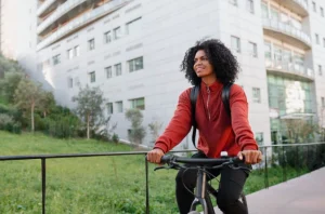 Pessoa de bicicleta em ciclovia ao lado de prédio moderno e área verde, destacando a importância desses espaços na paisagem urbana.