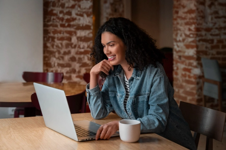 Mulher sentada em uma cafeteria, analisando as opções de apartamentos em seu laptop, em clima de concentração e pesquisa imobiliária.