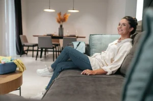Mulher jovem sentada confortavelmente em um sofá moderno dentro de um apartamento bem decorado, transmitindo a sensação de tranquilidade.