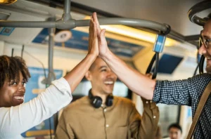 Duas pessoas se cumprimentando enquanto estão de pé em um trem, com clima descontraído e coletivo.