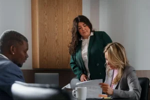 Três profissionais em reunião de negócios, sentados à mesa com documentos e notebook, discutindo contratos e estratégias de proteção jurídica e patrimonial.