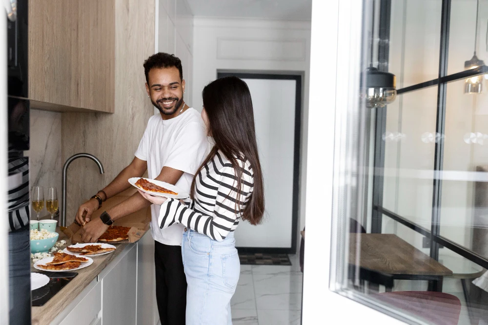 Casal jovem e sorridente na cozinha compacta de apartamento moderno.