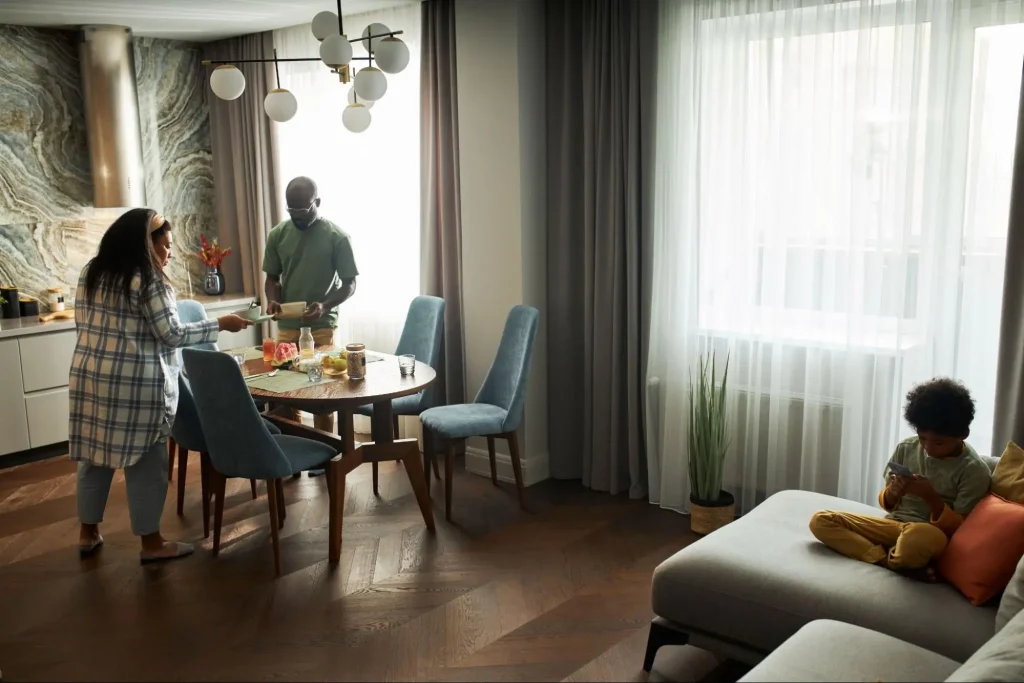 Família reunida na cozinha integrada de apartamento moderno. A mulher está de camisa xadrez, o homem de camisa verde e a criança relaxa no sofá cinza.